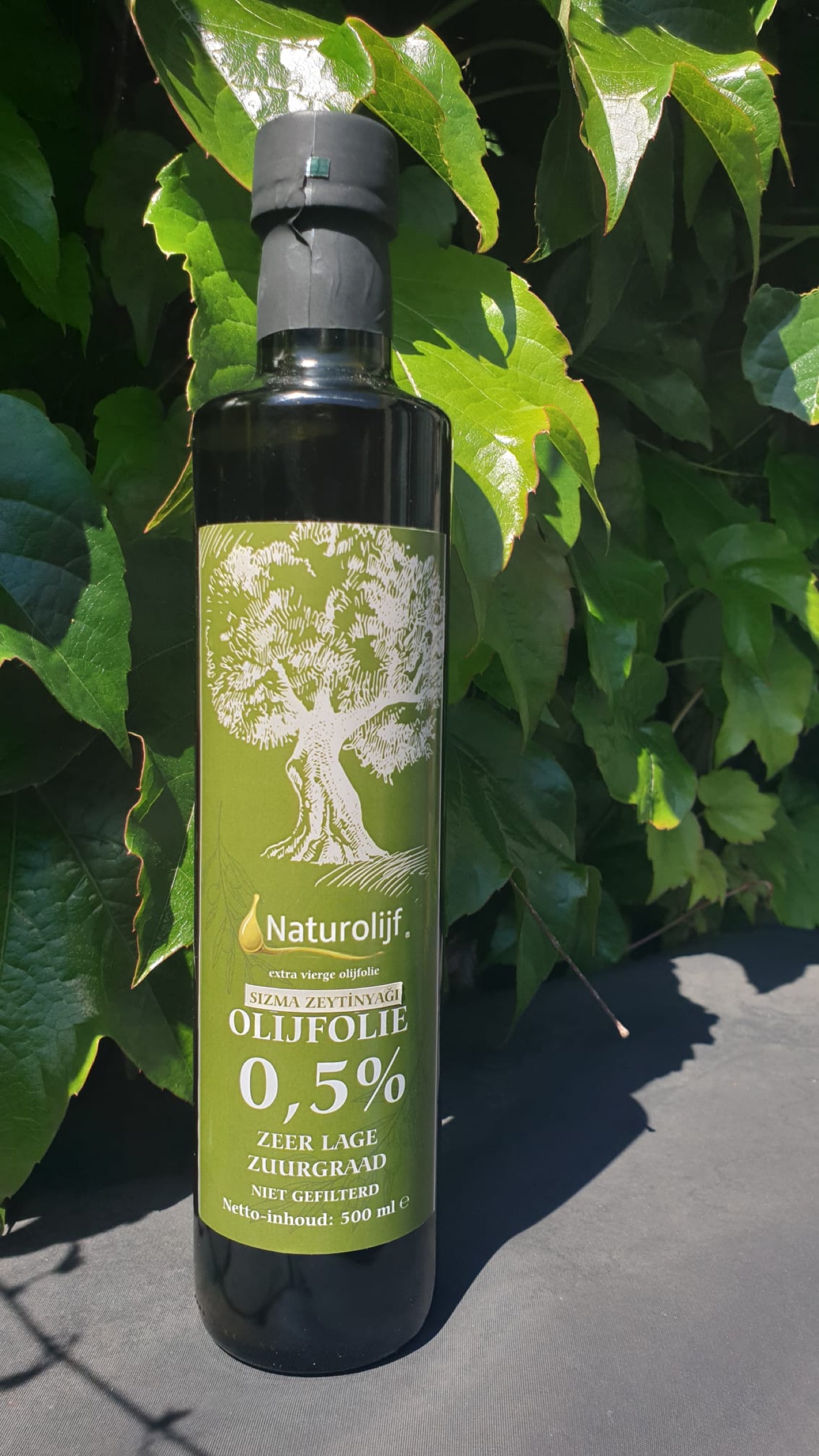 Fles Naturvia olijfolie, 0,5 procent zuurgraad, voor de groene bladeren van een wijngaard.